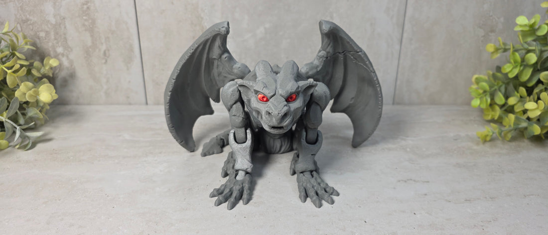 A gray 3D-printed gargoyle toy figurine with glowing red eyes and outstretched wings, positioned on a light gray surface against a tiled background.
